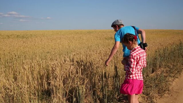 Boy and girl stand near yellow wheat field at summer day