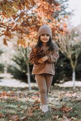 happy little brunette girl in a knitted hat walks in the park in autumn