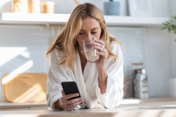 Young woman enjoying a cup of coffee while using her mobile phone in the living room at home.