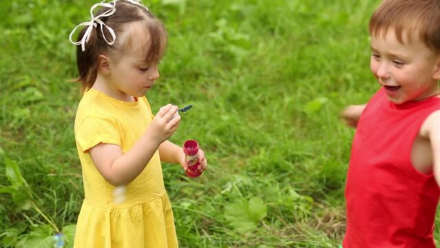 Little girl blows soap bubbles and boy plays with it on grass