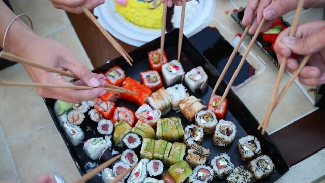 Hands with chopsticks on plate with a variety of sushi.