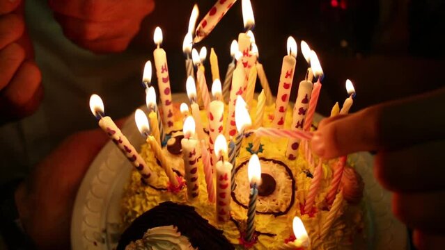 Hands burning candles on cake in dark close up at birthday party.