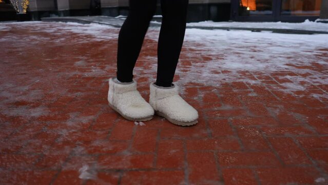 Close-up legs of unrecognizable woman wearing winter shoes walking on slippery city sidewalk. Closeup cropped shot of female walking along ice pavement. Danger season trauma. Shooting in slow motion.