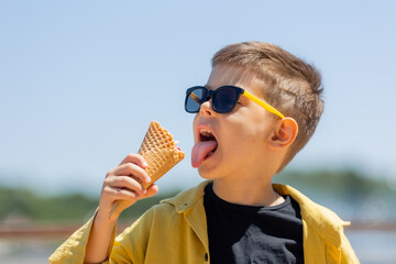 Happy little boy eats ice cream in a waffle cone in summer on a walk
