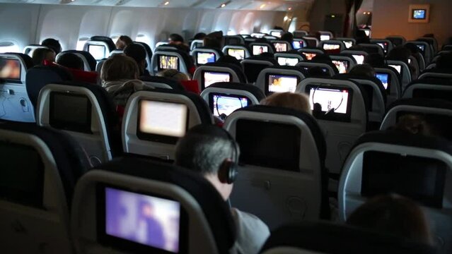 People at cabin of airplane. Backseats equipped with monitors.