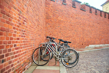 Bicycles are parked in a special parking lot near the large wall of the castle made of old red brick in the old streets of Europe in the center of Krakow.