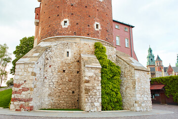 A building made of old red brick with lush green ivy climbing over it on the old Zamek Krolewski na Wawelu castle in the center of Krakow.