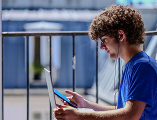 Nice photo of a young Caucasian man working with his laptop, earphones and mobile phone. He is...