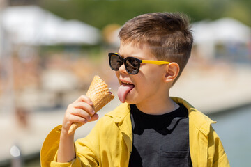 Happy little boy eats ice cream in a waffle cone in summer on a walk