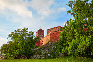 The old red brick Zamek Krolewski na Wawelu Castle is surrounded by green flowering plants in the center of Krakow.