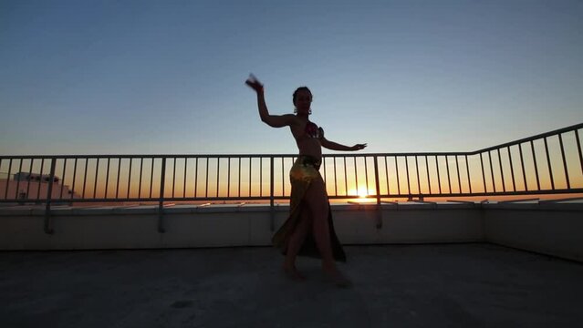 Beautiful woman dancing in Indian style in sunset on apartments roof.