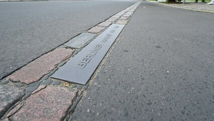 Berlin, Germany, August 10, 2023. Footage with a close-up image of the street: historical traces of the route of the wall have been left. A plaque commemorates the years in which it existed.