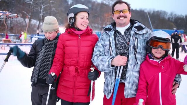 Family of four skiers smile at winter evening at track in ski resort