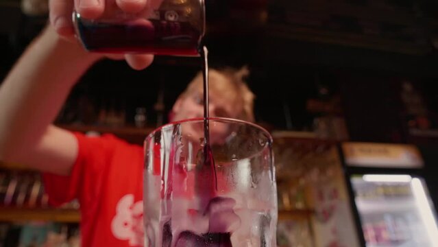 Professional bartender preparing a cocktail with ice a mix of violet syrup or alcohol. The barman measure quantities for a perfect cocktail and mixes all together with the spoon. bar or nightclub