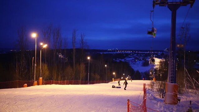 Snowboarders and funicular at night in skiing sports complex