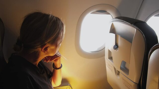 Passenger woman is flying in plane. Girl sitting in airplane looking out window going on trip vacation travel. Traveling female inside plane enjoying flight. Traveling girl