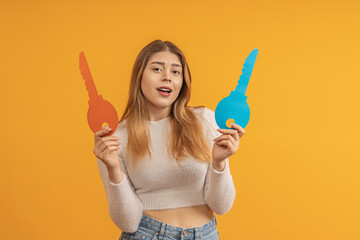 Woman holding a blue key cutout in one hand and an orange one in the other, looking surprised.