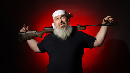 A man with a gray beard poses for the camera with his favorite weapon against the background of a...