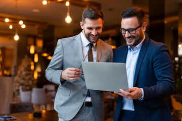 Two satisfied business men looking at a slideshow presentation on a laptop in a co-working space.