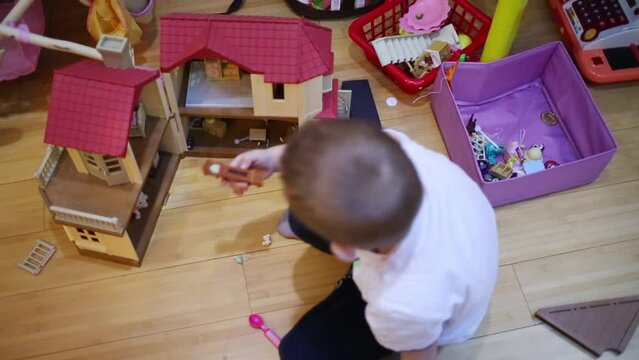Boy playing with toy house sitting on wooden floor