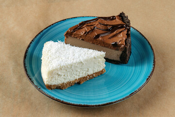 A slice of coconut cheesecake and a slice of chocolate cheesecake on a blue plate.