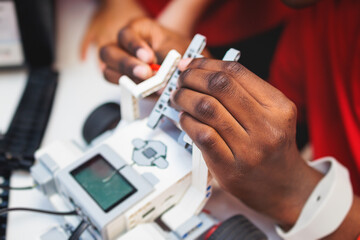 Group of diverse children kids with robotic vehicle model, close-up view on hands, science and engineering lesson in a classroom, making, coding and programming a robot in a school, robotics projects