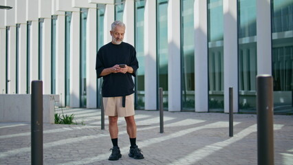 Retired man typing smartphone at downtown. Pensive mature male using mobile