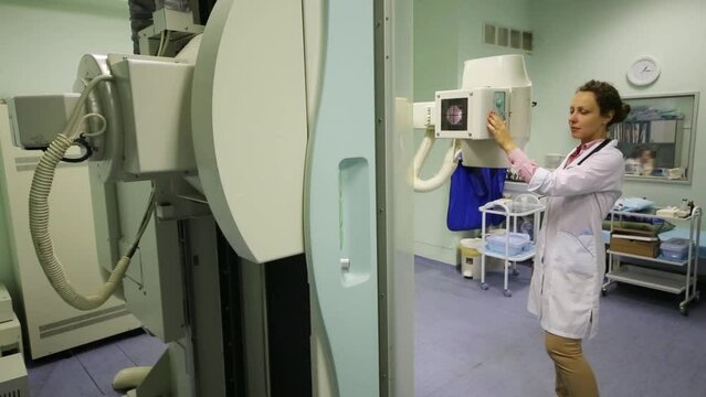 A woman in a white coat setting up x-ray machine in clinic