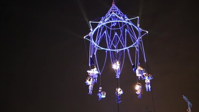 Actors on spinning metal framework made in shape of giant chandelier