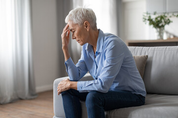 Depressed european senior lady suffering from headache touching head indoors