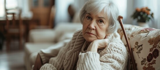 A grey-haired woman with a walking stick resting on a sofa at home, with selective focus.