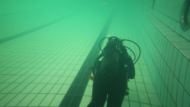 Back of diver in wetsuit with scuba swimming on bottom of pool