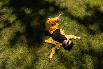 Happy little boy in sunglasses lying on the lawn in summer, top view