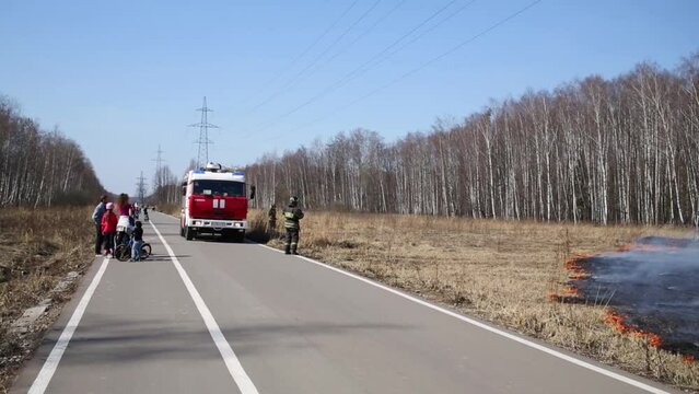 Firefighters around fire truck going to extinguish burning grass 