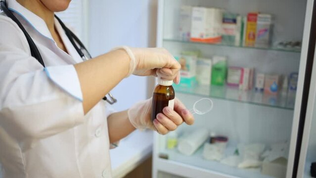 Female doctor in white lab coat opens bottle of medicine syrup.
