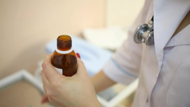 Doctor in white lab coat opens bottle of medicine syrup.