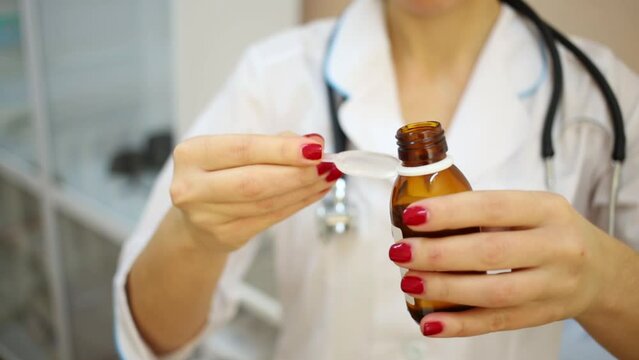 Female doctor pours medicine syrup into plastic measuring spoon.