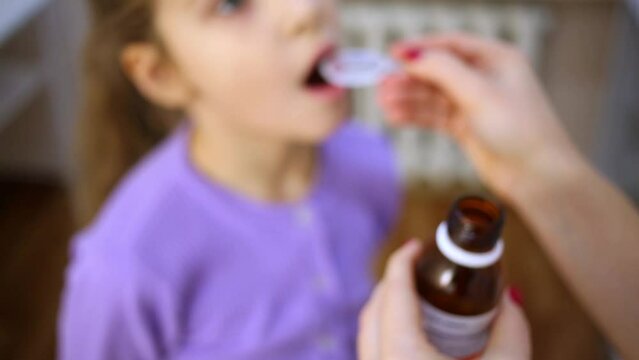 doctor pours medicine syrup into measuring spoon and gives it girl.