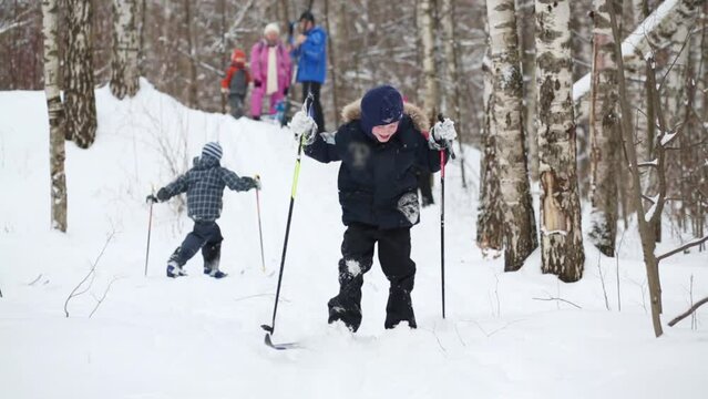 Boy slides on skis from hill next to two adults and three children