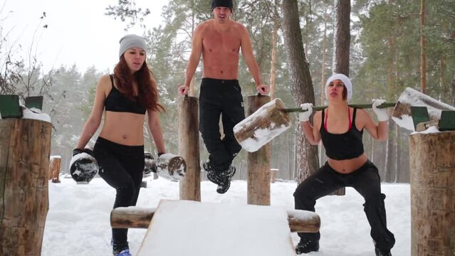 Two girls do squats with wooden dumbbells and guy parallel bars dips