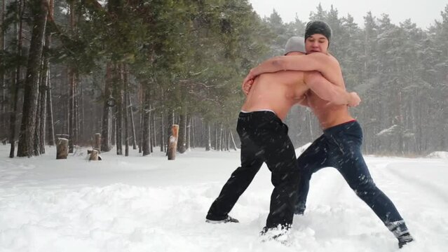 Two guys wrestle standing at outdoor sportsground in winter wood.