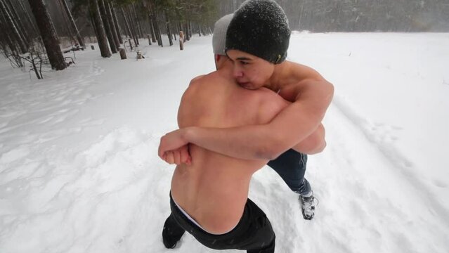 Two guys wrestle standing at outdoor sportsground in winter forest.