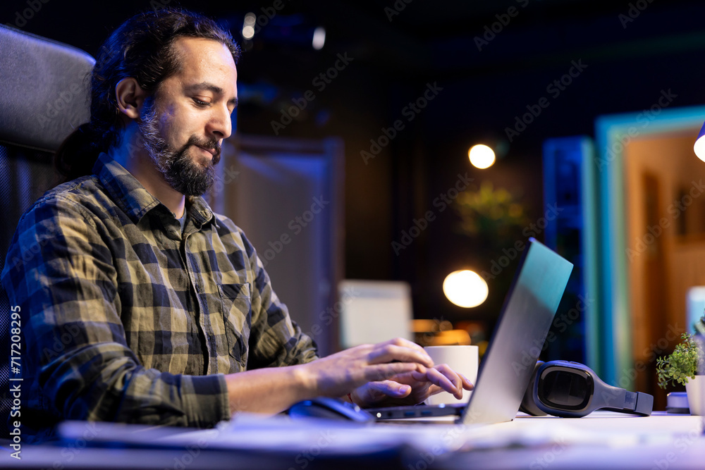 Aufkleber man using a laptop to type and browse the internet at his living room desk. young male adult is focu