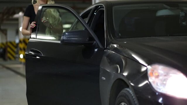 Beautiful blonde woman opens and closes door of black car