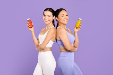 Two diverse women in activewear holding juice bottles, back to back