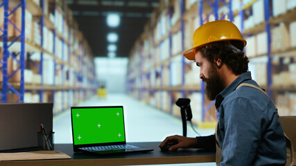 Customs compliance officer uses greenscreen pc in warehouse, looking at isolated chromakey display. Male depot employee working with package shipment and blank copyspace template.