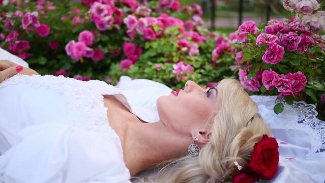 Woman in white dress lying on grass among flowerbeds with roses.