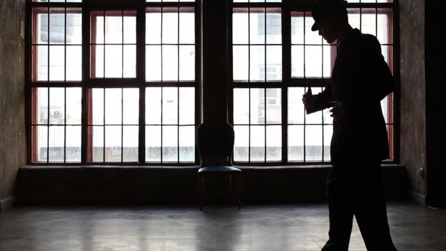 Silhouette of man in black suit and hat dancing tango near window