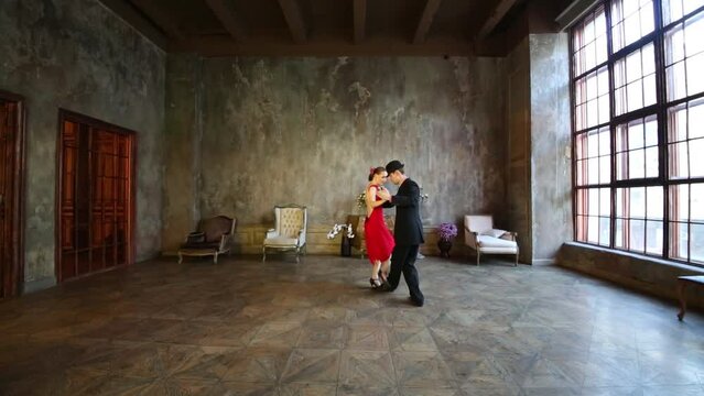 Girl in red dress and man in black suit dance tango in retro room