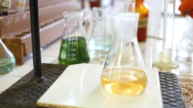 Hands in gloves drips liquid into flask with yellow liquid